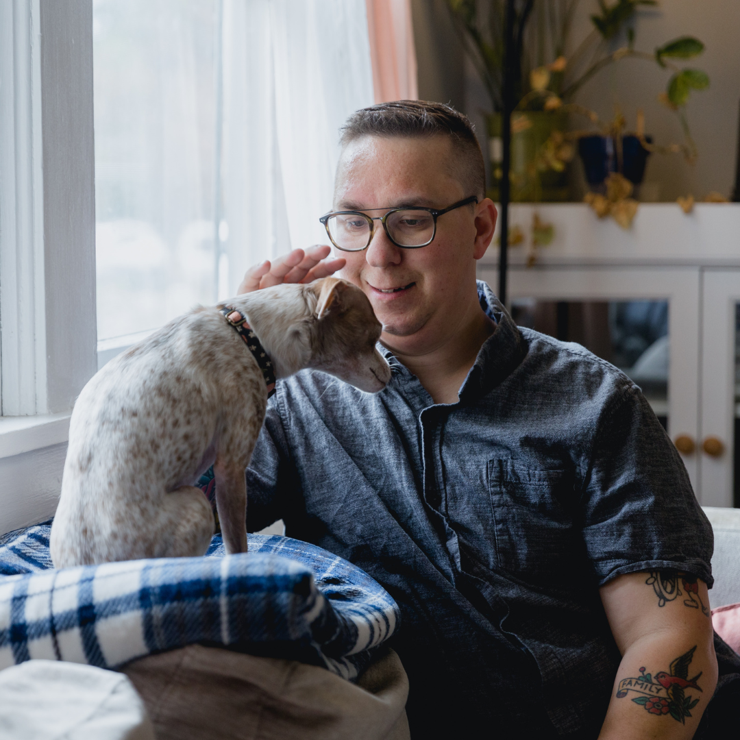 A man sits on a sofa petting his dog who is sat in front of him
