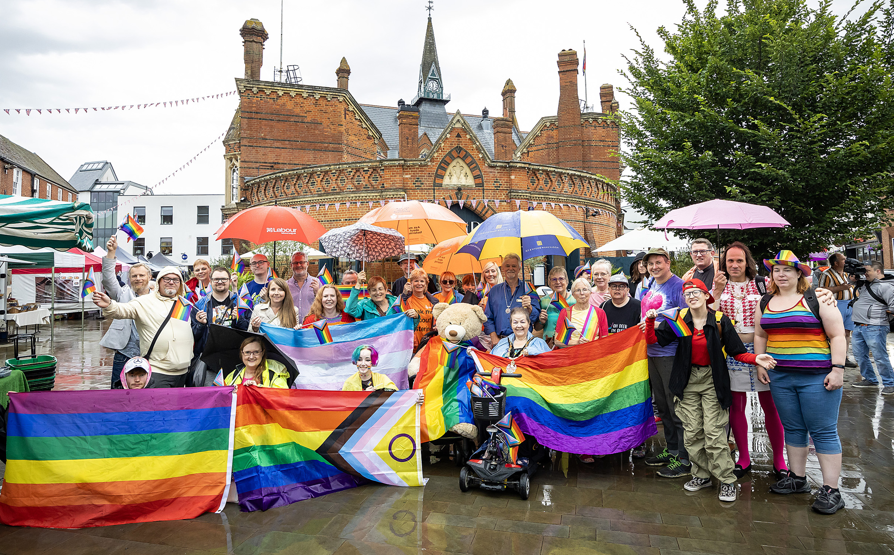 A group of diverse people holding rainbow flags and celebrating Pride in Wokingham market place