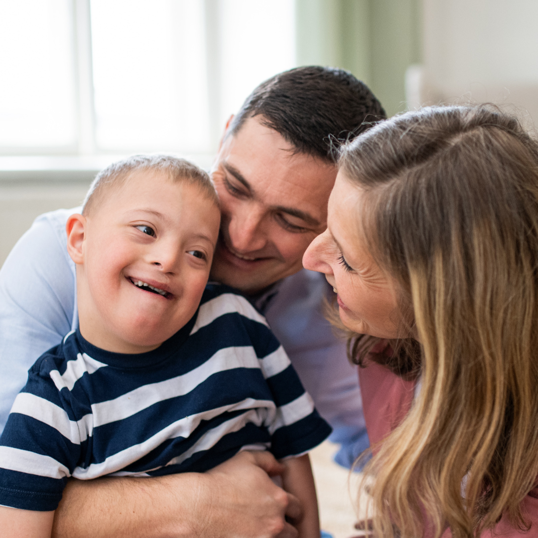 A young boy sitting smiling with two adults