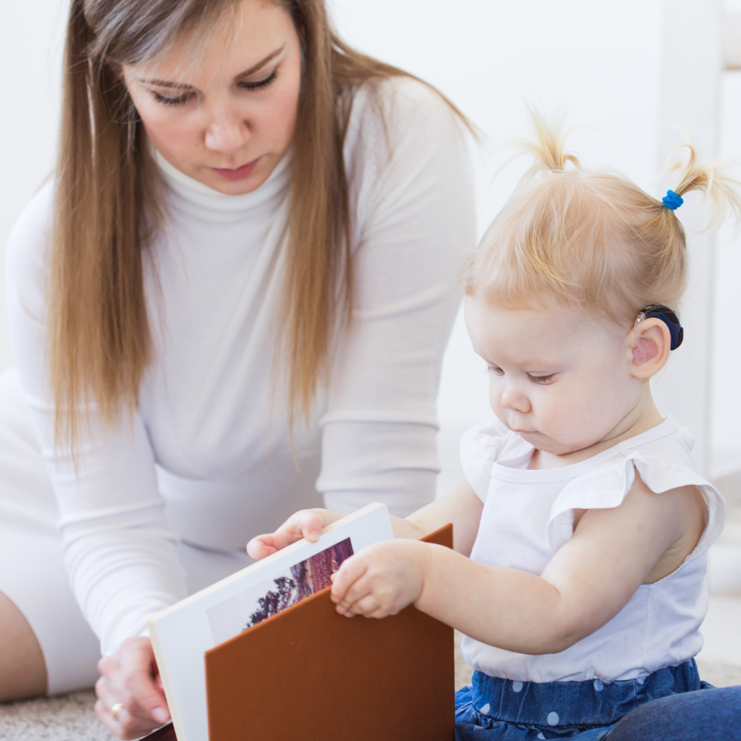 Young girl with a hearing aid looks at a book with a woman
