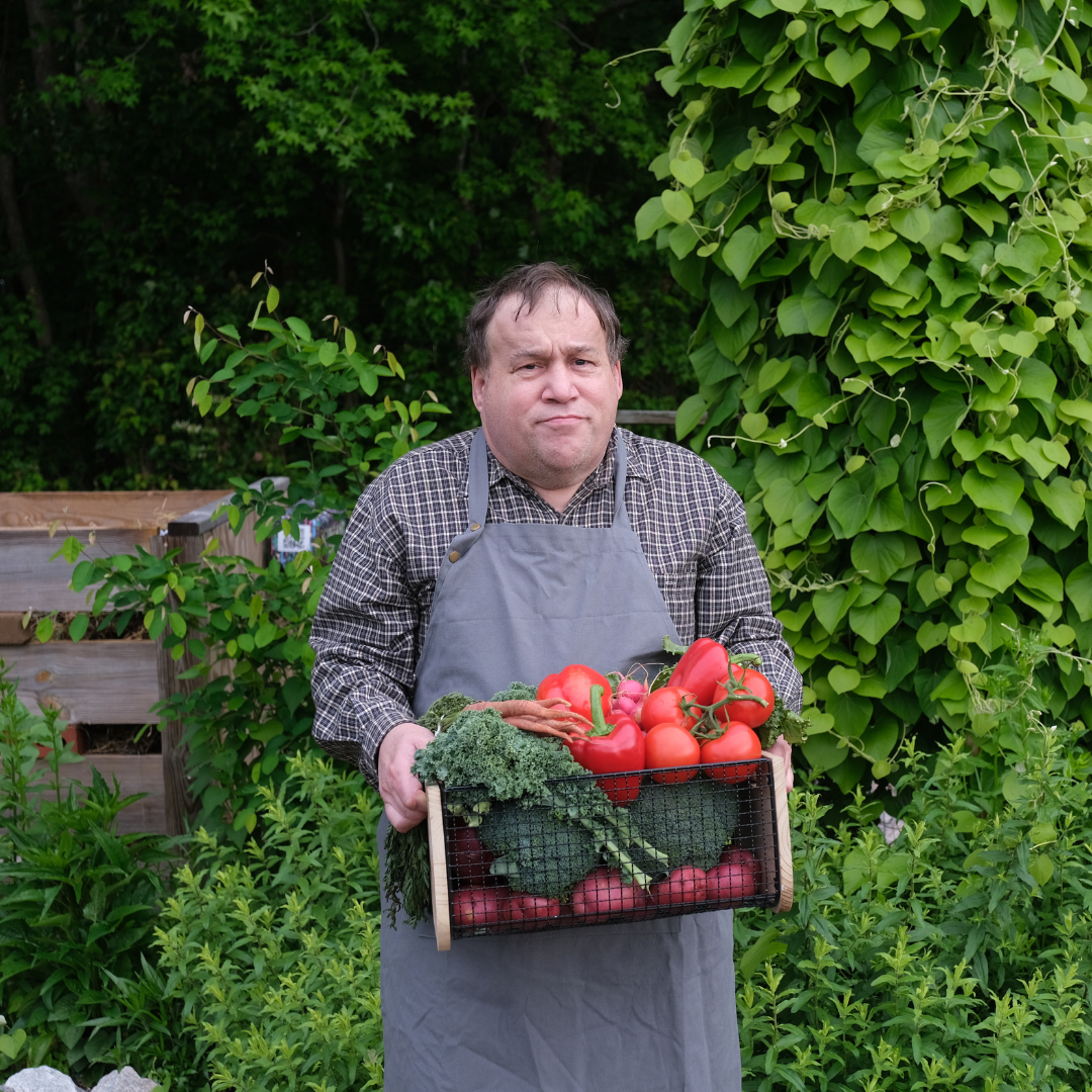 A man in a garden carrying a basket of vegetables