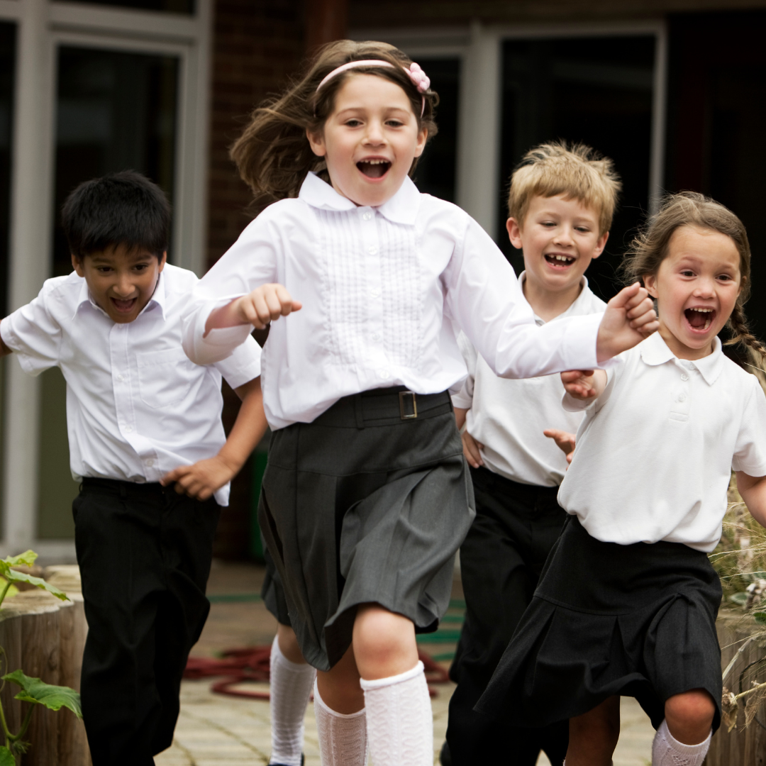 Four children in school uniform run towards the camera laughing