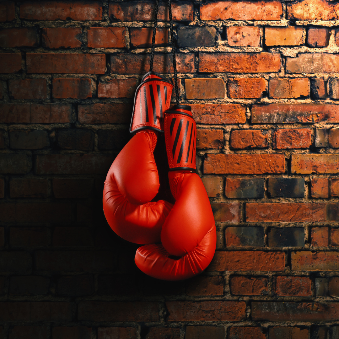 Red boxing gloves hanging up against a brick wall