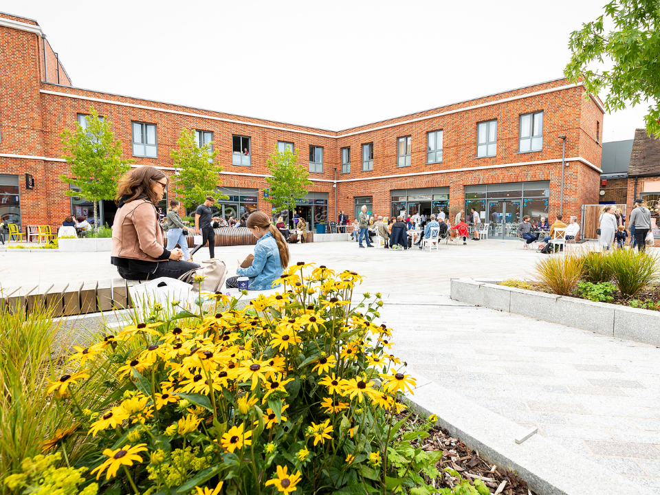 A clean, bright pedestrianised shopping area on a sunny day with a flower bed in the foreground
