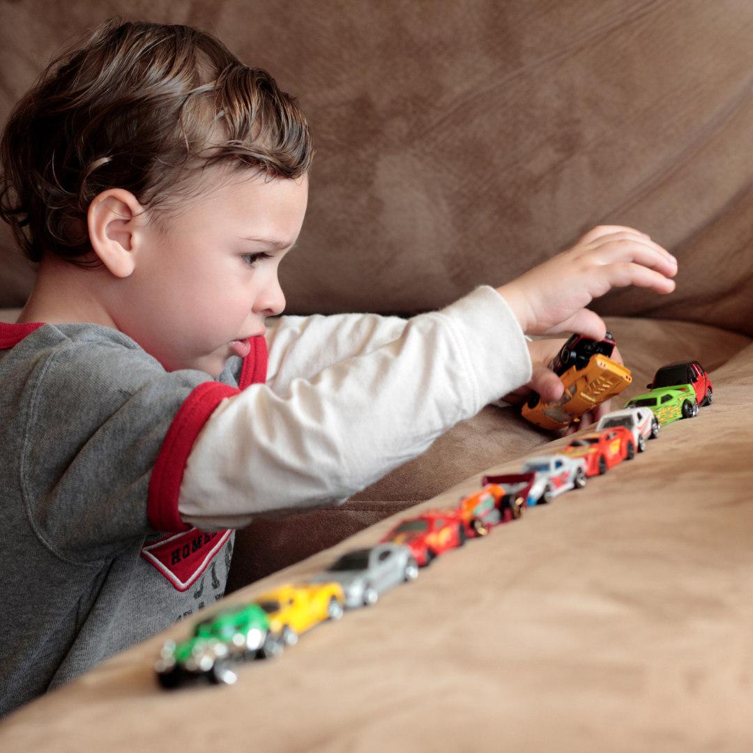 A young boy lines up toy cars on a sofa