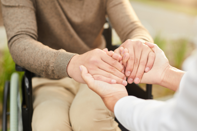 Photo of a person in a wheelchair holding hands with another person