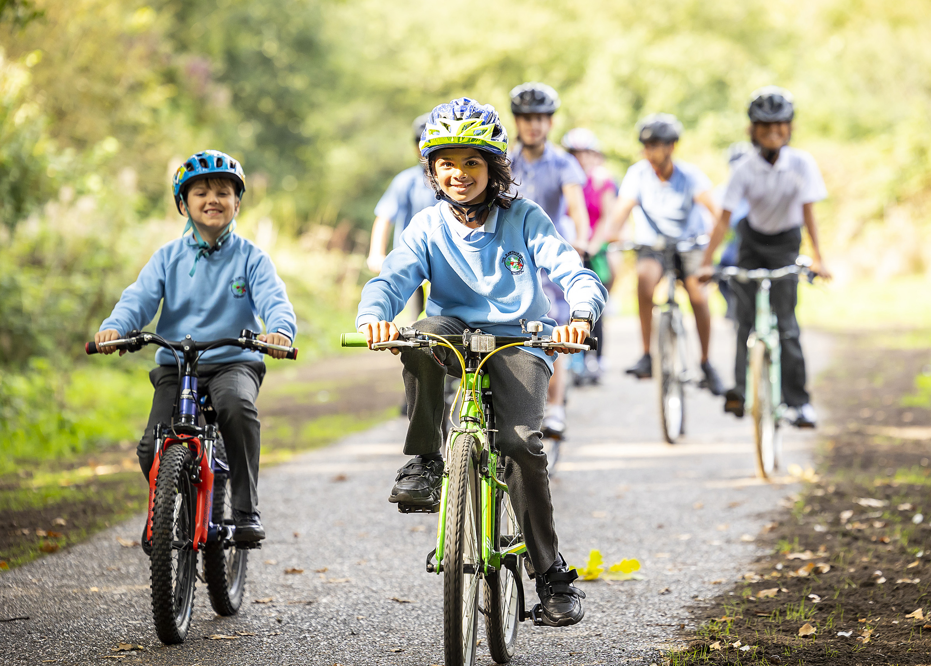 Children wearing cycling helmets cycling on a path through a wooded area