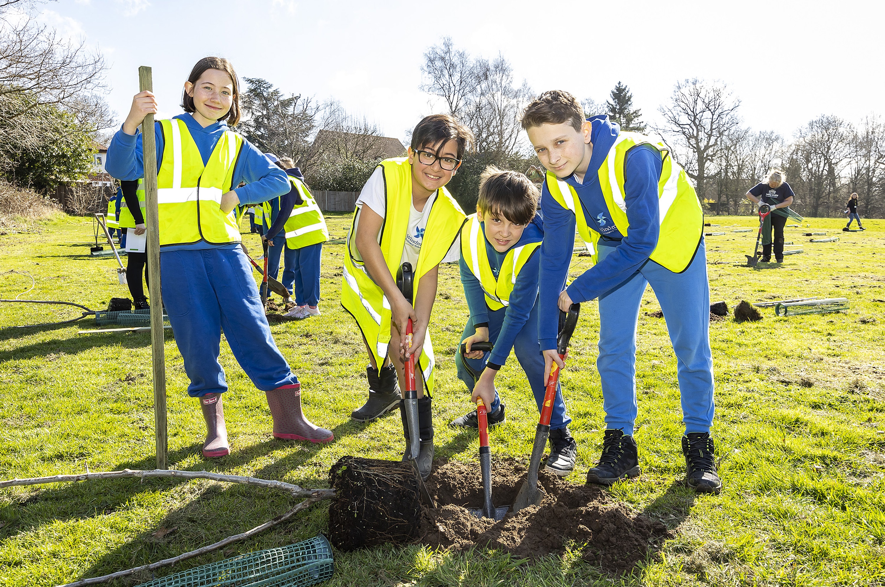 four smiling children wearing high viz vests digging a hole to plant a tree