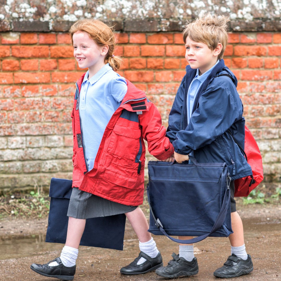 Two children in school uniform walking along a pavement carrying school bags