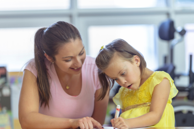 Girl drawing with adult pointing at paper