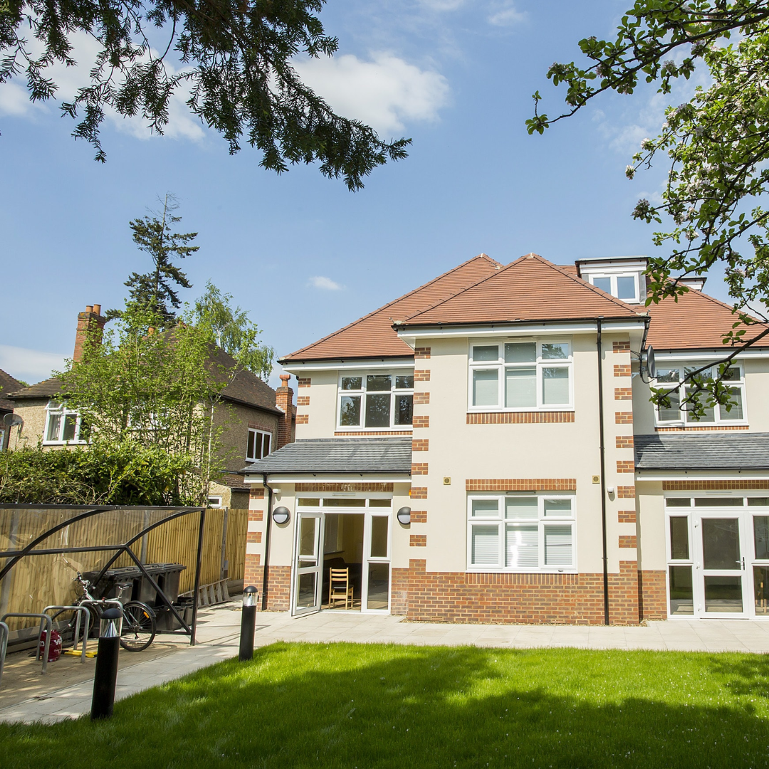 The back of one of our young people accommodation, showing a grass area, bike racks and a large residential looking house