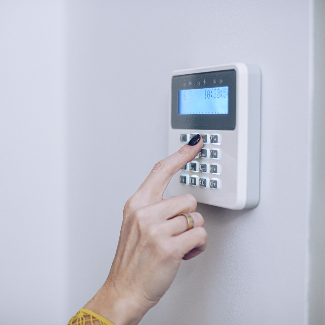 A hand keying in a number on an electronic burglar alarm