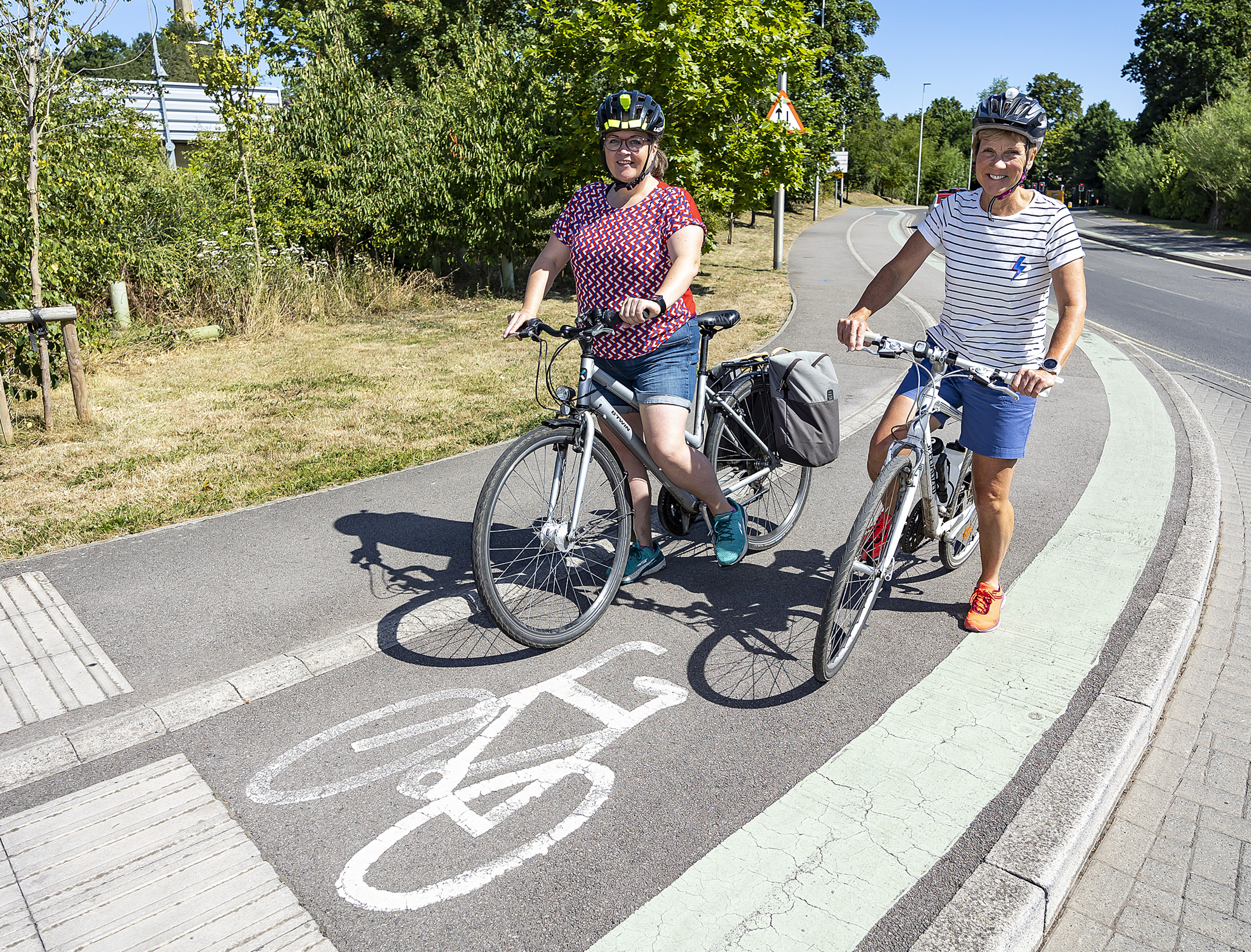 Two women on bikes smile for the camera while posing on a segregated cycle track