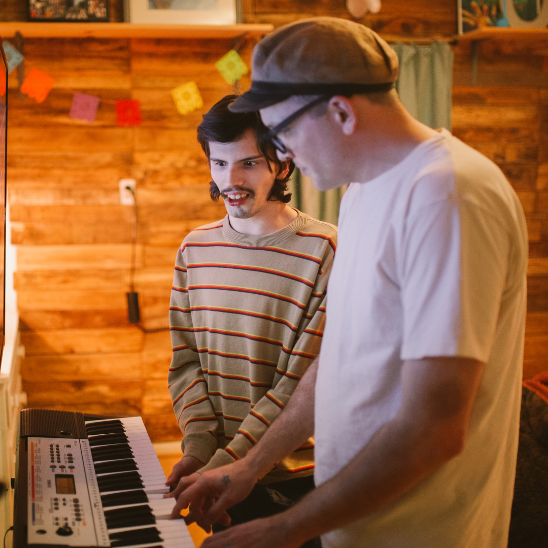A man showing another man how to play the keyboard
